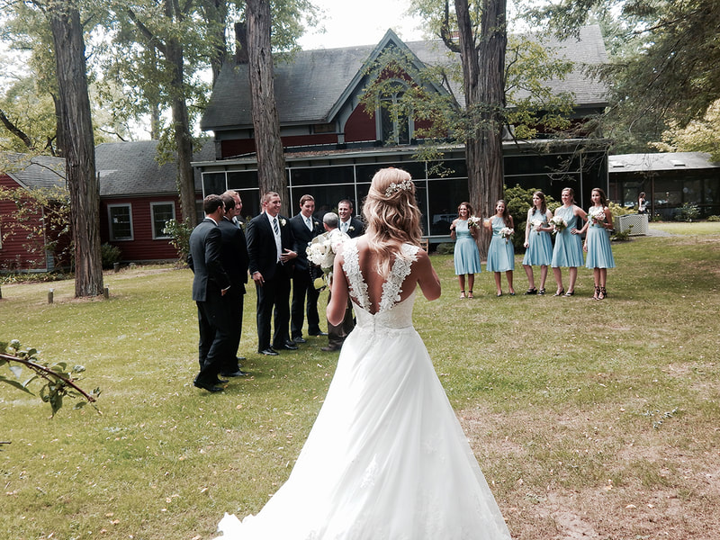A photo of a wedding at Garvan's in New Paltz. The bride's back, looking toward the wedding party with Garvan's in the background